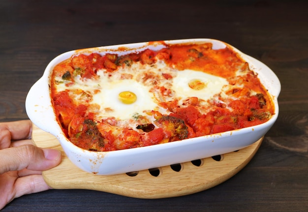 Photo plaçant à la main un bol de shakshuka fraîchement cuit sur la table de la cuisine