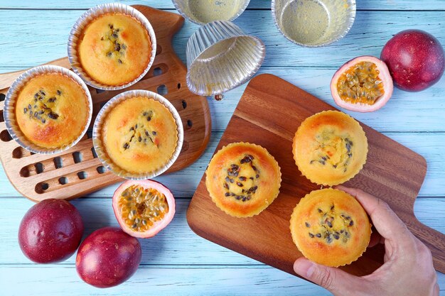 Placer à la main des muffins aux fruits de la passion faits maison et cuits au four sur une planche à découper en bois sur fond bleu