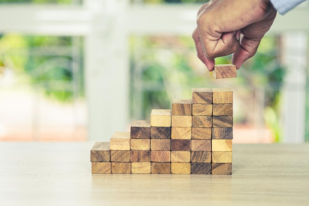 Placer à la main la pile de tours de blocs de bois dans l'escalier pyramidal avec prudence pour éviter l'effondrement ou l'écrasement des concepts de gestion des risques financiers, de planification stratégique et de plan de défi commercial