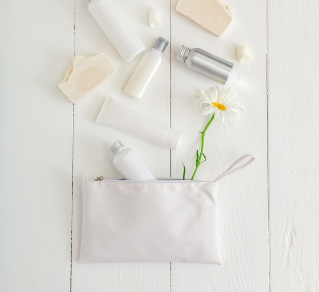 Placez les produits cosmétiques blancs sur la table en bois avec des fleurs dans le sac cosmétique. Beauté soins de la peau traitement capillaire sérum cosmétique huile hydratant crème pour la peau corps beurre savon lotion shampooing. Mise à plat.