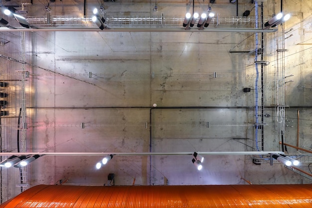 Plafond en béton gris avec spots halogènes et lampes edison dans la salle de bureau loft avec climatisation et tuyau de ventilation orange jusqu'à