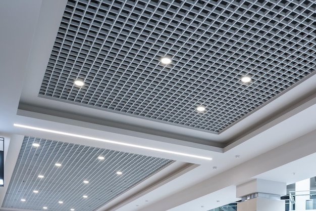 Plafond suspendu et grillagé avec lampes halogènes et construction de cloisons sèches dans une pièce vide d'un magasin ou d'une maison Plafond tendu blanc et de forme complexe