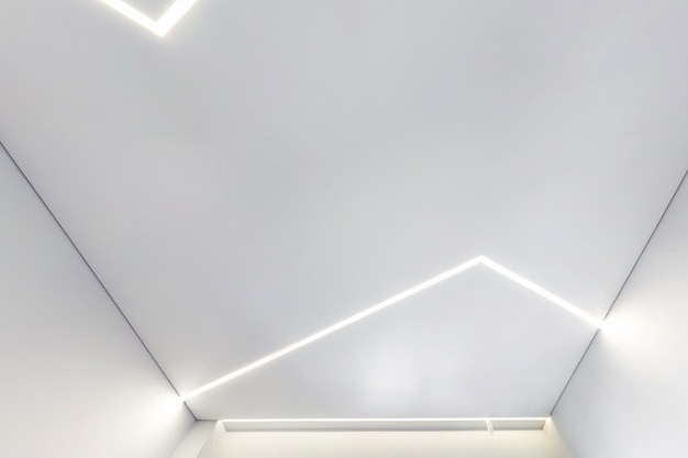 Plafond suspendu avec lampes halogènes et construction de cloisons sèches dans une pièce vide d'un appartement ou d'une maison Plafond tendu blanc et de forme complexe