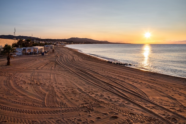 La plage de Badalona au lever du soleil avec des traces de pas et des traces de voiture sur le sable