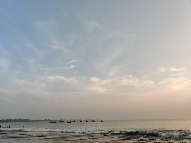 Une plage avec un ciel nuageux et quelques bateaux à l'eau.