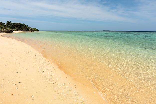 Plage confortable, mer vert émeraude, sables lisses, rochers côtiers, île en arrière-plan.