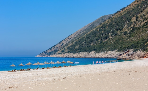 Plage du matin d'été avec eau aigue-marine, transats et parasols en paille (Albanie).