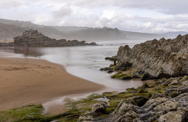 PLAGE DU NORD AVEC DES VAGUES ET DES ROCHERS SOUS UN CIEL NUAGEUX DE PRINTEMPS