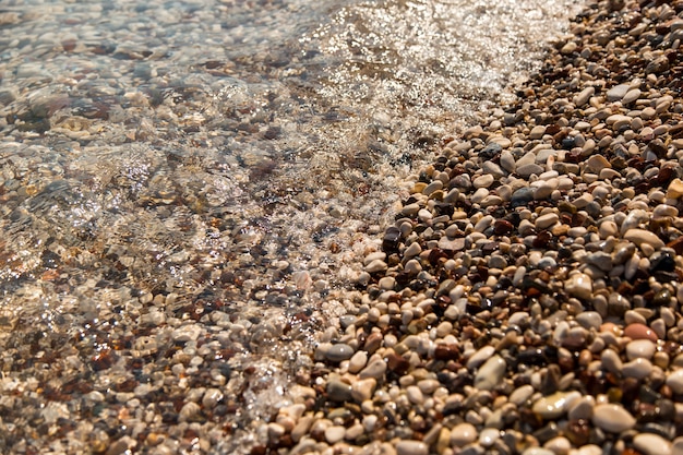 La plage est faite de galets, le bord de mer, de petits galets colorés dans l'eau. Arrière-plan, copiez l'espace.