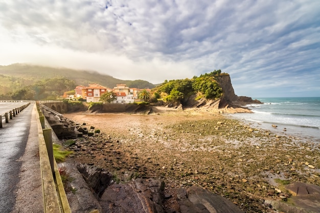 Plage de galets avec maisons en bord de mer, falaises et ciel dramatique avec cumulus. Vizcaya, Pays Basque. Espagne