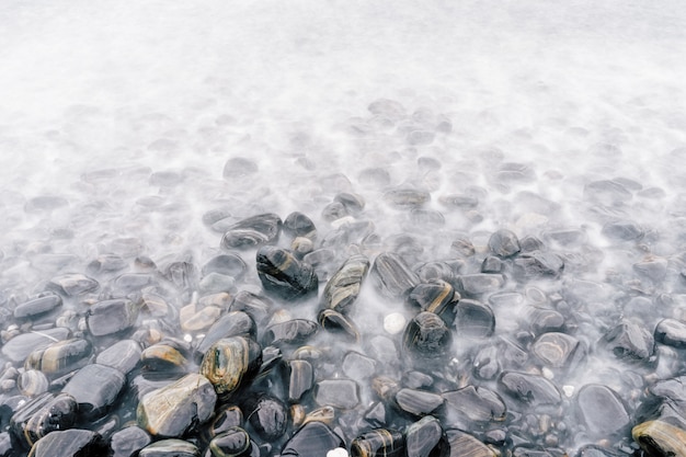 Plage de galets de mer avec pierres multicolores, vagues transparentes avec brouillard