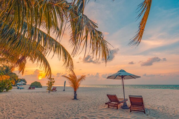 Plage idyllique au coucher du soleil. Belle île tropicale rivage couple lits de plage parasol sous les feuilles de palmier