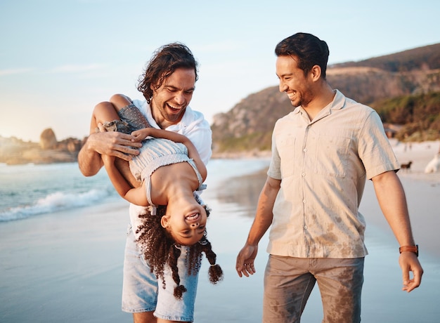 Plage lgbtq et parents jouent avec une fille en été pendant les vacances et l'aventure Famille heureuse, relation saine et enfant avec des pères homosexuels au bord de l'océan pour créer des liens, se détendre et s'amuser en plein air