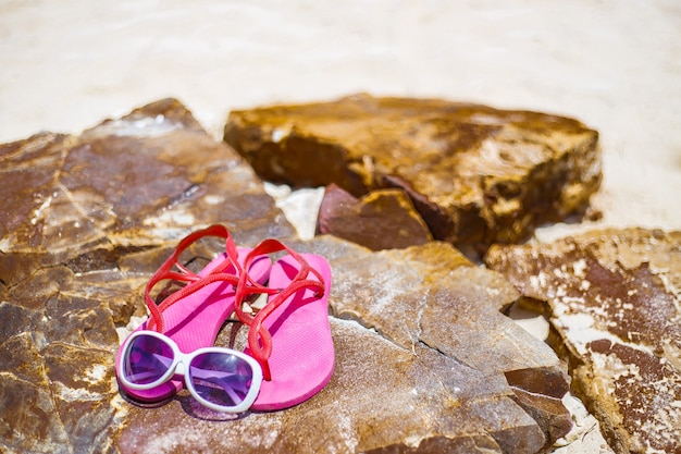 La plage avec des lunettes de soleil et des sandales sur le rocher, espace de copie pour le texte.
