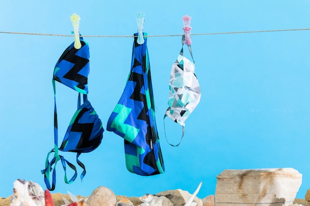 Sur la plage, un maillot de bain et un masque protecteur contre le ciel bleu sont séchés sur une corde.