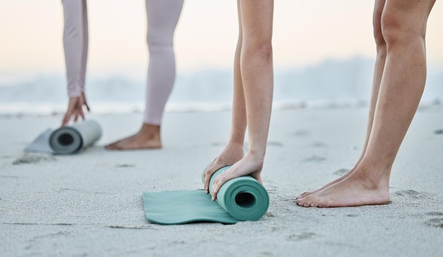 La plage de remise en forme et les femmes roulent un tapis de yoga pour se préparer à l'exercice d'entraînement ou à l'étirement de la méditation zen ou des mains de femmes filles ou d'amis à l'extérieur sur un tapis roulant de sable de plage pour l'entraînement de pilates