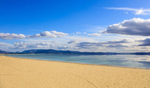 Plage de sable mer calme ciel bleu avec quelques nuages blancs fond Destination d'été Réflexion sur la mer de nuages et de montagnes