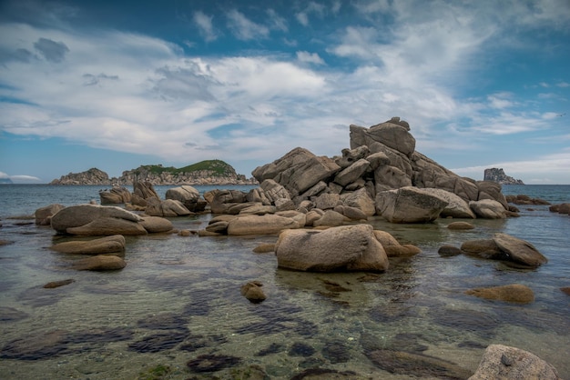 Une plage de sable de mer avec de grands rochers sur elle, des falaises sur le rivage et de l'eau claire.