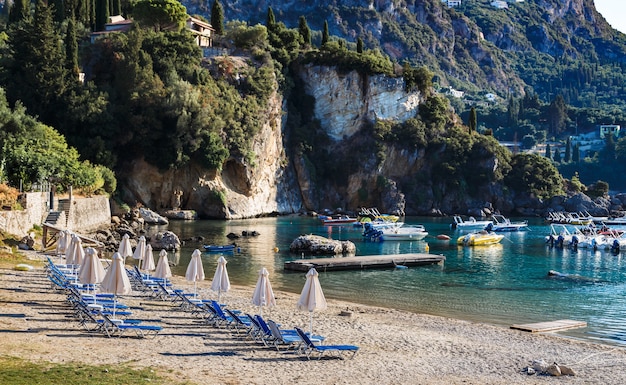 Plage de sable à Paleokastritsa Corfou Grèce le matin transats parasols bateaux eau cristalline