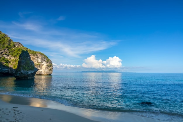 Plage tropicale et falaises envahies d'arbustes. Ciel bleu et nuages au-dessus de l'horizon. Ombre de l'après-midi