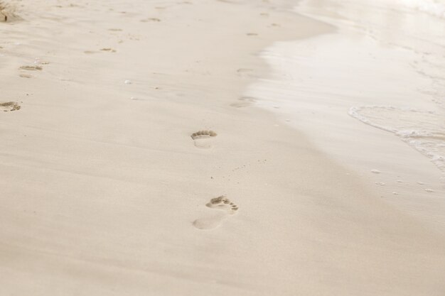 Plage, vague et empreintes de pas au coucher du soleil