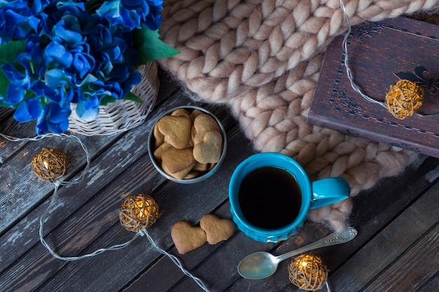 un plaid, un livre, une tasse de thé bleu, une guirlande et des biscuits