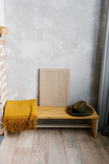 Plaid marron, chapeau de feutre et toile sur un banc en bois à l'intérieur d'une maison minimaliste scandinave