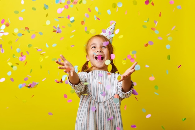 Plaisir d'anniversaire Petite fille joyeuse et heureuse avec des confettis sur fond jaune coloré