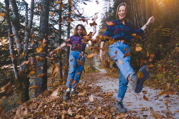 Plaisir d'automne. Deux filles heureuses dans la forêt jettent des feuilles sèches