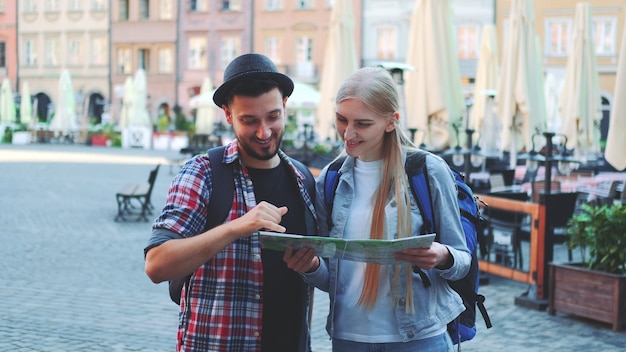 Plan agrandi de touristes tenant une carte et souriant à la caméra. Ils se tiennent sur une grande place du marché de la vieille ville européenne.