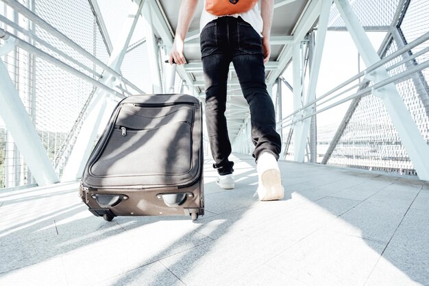 Plan arrière d'un voyageur transportant ses bagages et sacs à l'aéroport ou à la gare routière lors d'un voyage. Voyageur moderne hipster, journée ensoleillée, espace de copie.