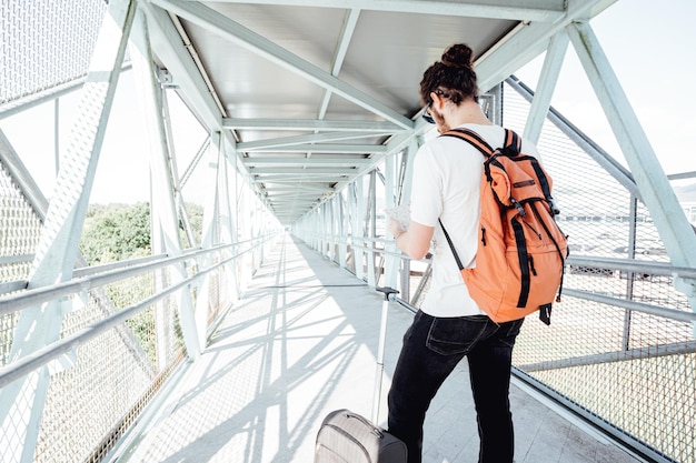 Plan arrière d'un voyageur vérifiant une carte alors qu'il transportait ses bagages et ses sacs à l'aéroport ou à la gare routière pendant un voyage. Voyageur moderne hipster, journée ensoleillée, espace de copie.