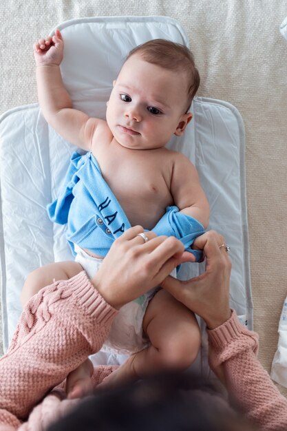 Plan d'un bébé souriant s'amusant avec sa mère tout en changeant sa couche à la maison.