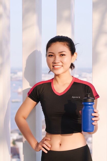 Plan d'une belle coureuse tenant une bouteille d'eau. Femme de remise en forme prenant une pause après avoir exécuté une séance d'entraînement en plein air.