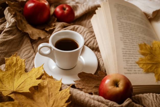 Plan de café expresso près d'un livre ouvert avec une feuille d'érable jaune comme signet entouré de pommes rouges