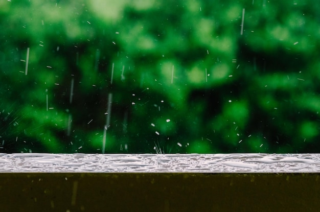 Plan cinématographique de gouttes de pluie tombant du ciel gris et sur la surface humide d'une balustrade de balcon créant des ondulations dans l'eau calme