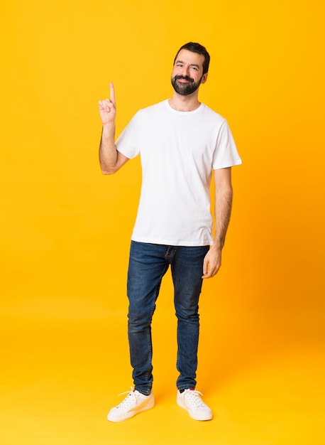 Plan complet d'un homme à la barbe sur fond jaune isolé montrant et en levant un doigt en signe de la meilleure