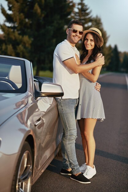 Plan complet d'un homme souriant penchant le cabriolet étreignant sa petite amie et regardant la caméra