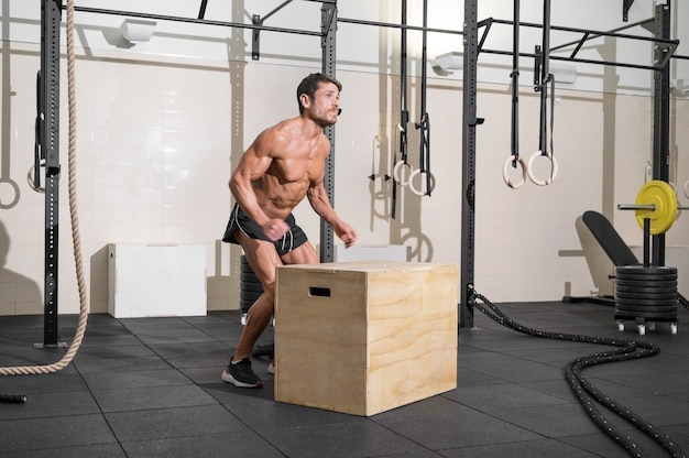 Plan complet d'un jeune sportif caucasien en forme s'entraînant seul à faire des exercices de saut de boîte dans la salle de sport