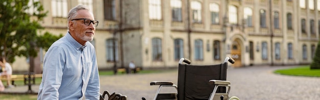 Plan complet d'un patient mature en convalescence avec fauteuil roulant assis sur le banc dans le parc près