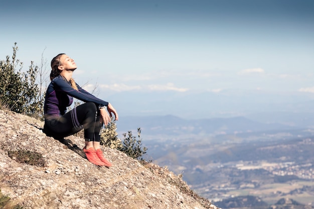 Photo plan d'un coureur de sentier assis et prenant une pause en regardant le paysage depuis le sommet d'une montagne.