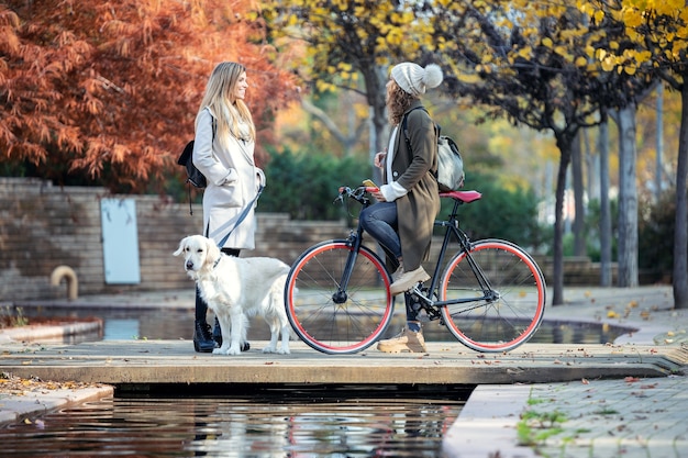 Plan de deux belles amies discutant en marchant avec leur chien et leur vélo sur un pont en automne.