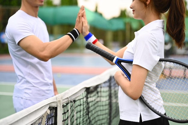 Plan de deux jeunes joueurs de tennis se donnant un high five au filet sur un court de tennis