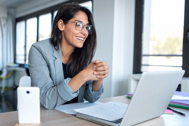 Plan d'une femme d'affaires confiante regardant et parlant à travers la webcam tout en faisant une vidéoconférence avec un ordinateur portable depuis le bureau.