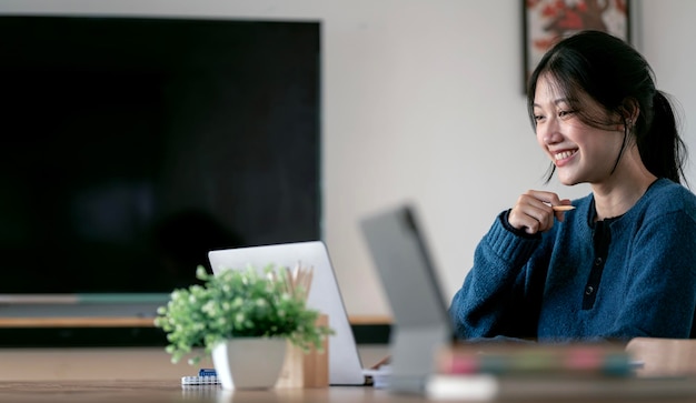 Plan d'une femme confiante assise derrière son ordinateur portable et ayant un appel vidéo tout en travaillant à domicile