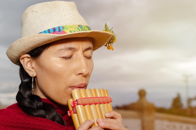 Photo plan fermé d'une femme indigène d'amérique latine avec un chapeau jouant de la zampona les yeux fermés