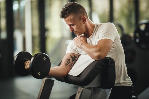 Plan d'un gars musclé en vêtements de sport qui s'entraîne dur dans la salle de sport. Il gonfle les muscles du biceps avec un poids lourd.