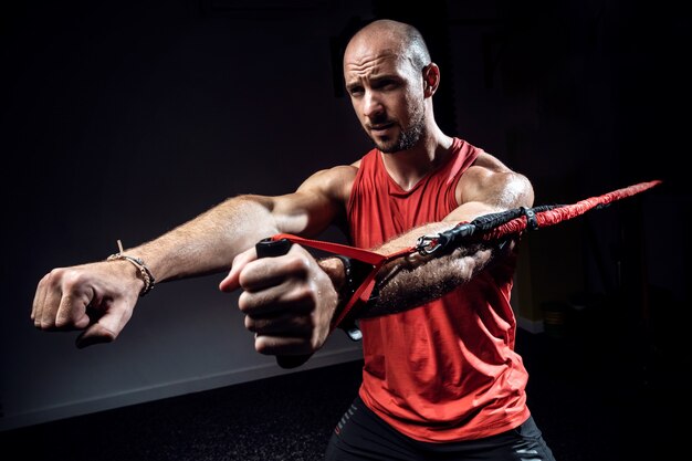 Photo plan d'un homme musclé pendant l'entraînement avec des sangles de suspension trx sur un studio sombre.