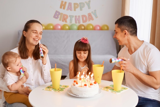 Plan horizontal d'une famille souriante et satisfaite assise à la table et célébrant l'anniversaire célébrant l'anniversaire de l'enfant ensemble à la maison exprimant le bonheur