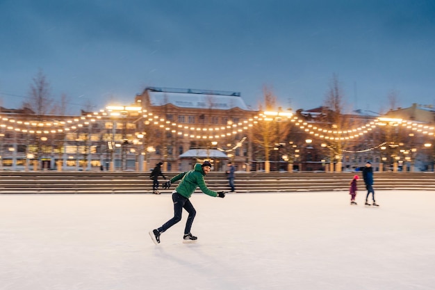 Plan horizontal d'un homme actif utilise des patins à glace pour faire du sport sur un anneau de glace passe des vacances d'hiver fait activement preuve de professionnalisme et de vitesse Patinage sur glace masculin à l'extérieur